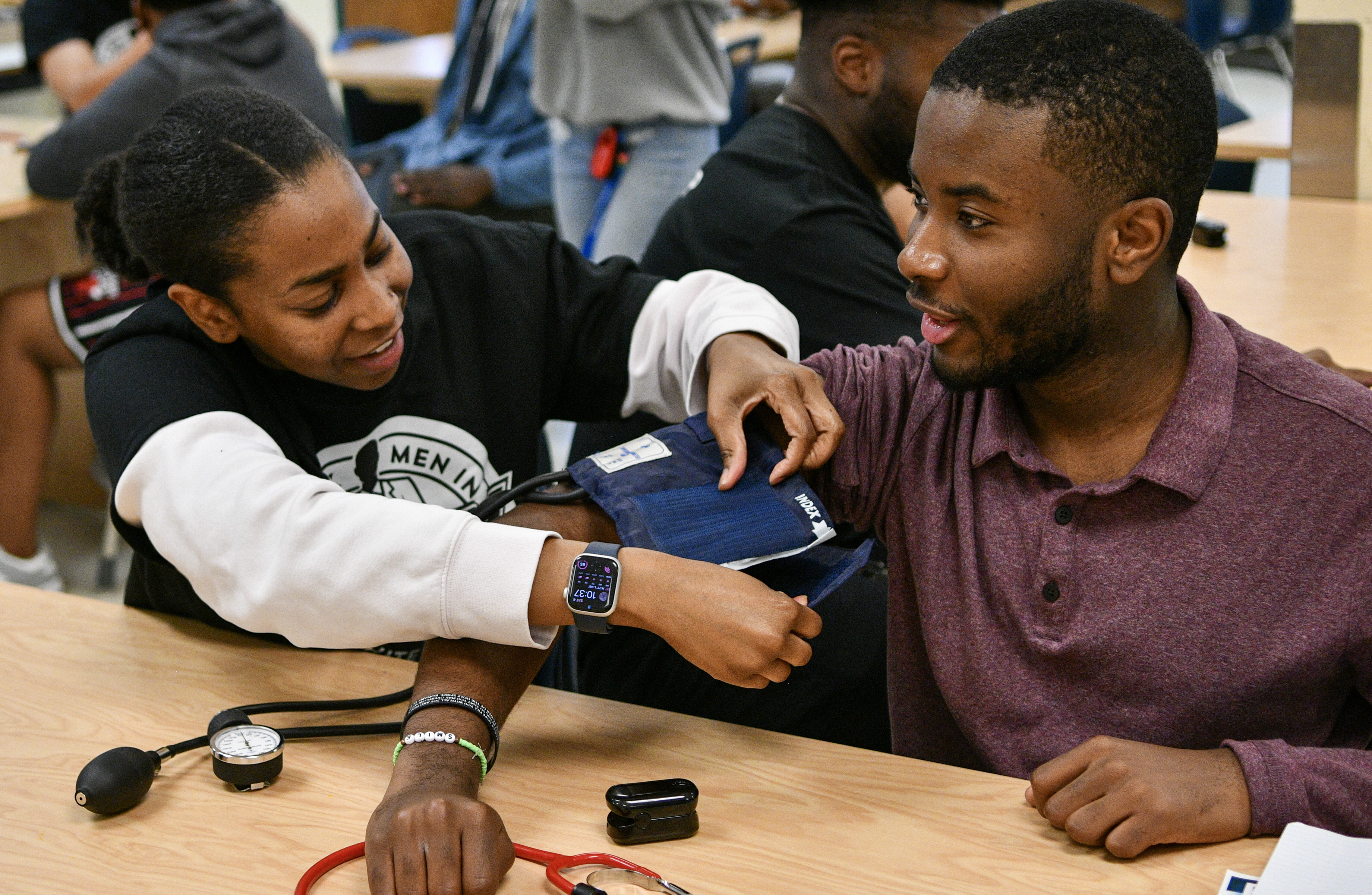A student practices putting a blood pressure cuff on another student.