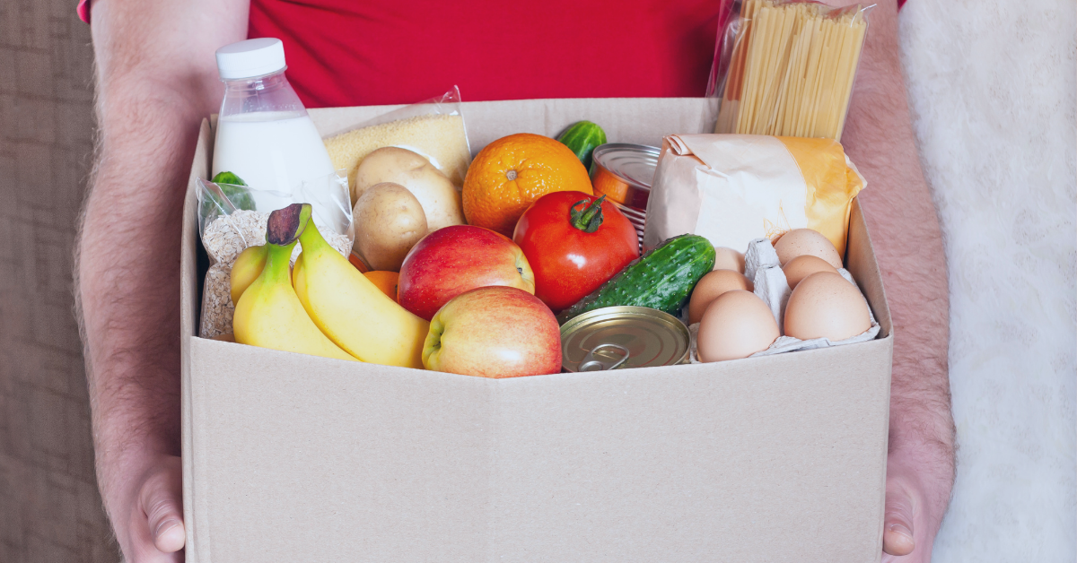 A man holds a box of fruits, vegetables, and other nutritius food items.