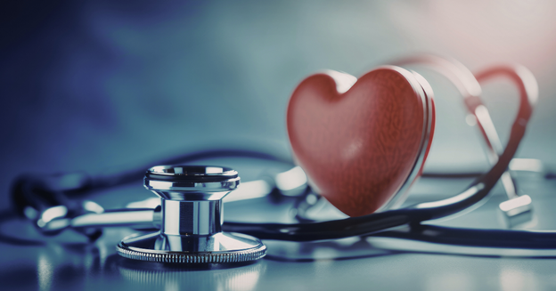 A heart sits next to a stethoscope on a table surfac.e