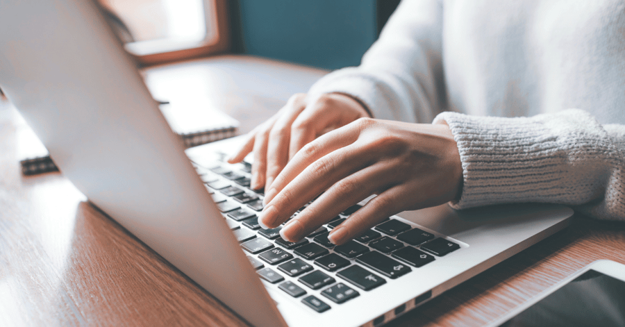 Hands type on a laptop keyboard.