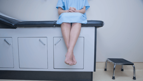 A female patient wearing a hospital gown sits on an exam table.