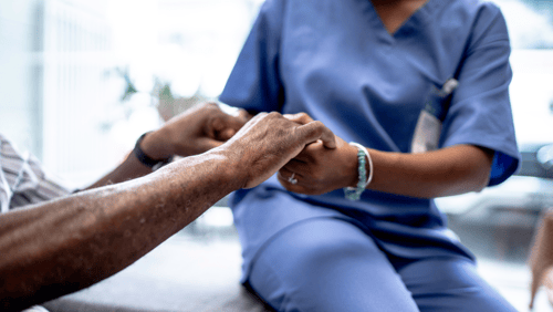 A medical assistant holds hands with a patient.