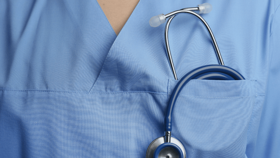 A close-up of a stethoscope lying against the chest of someone wearing blue medical scrubs.