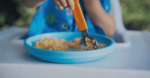 A child uses a spoon to push food around on their plate.