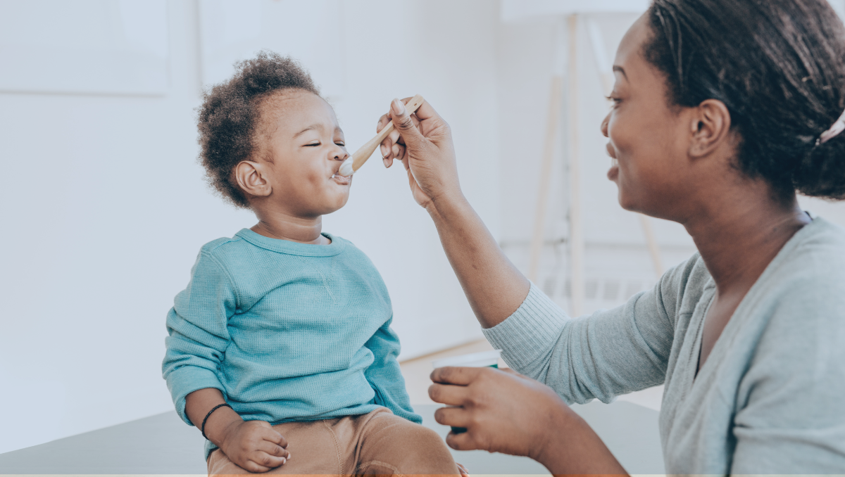 A mom feeds her toddler with a spoon.