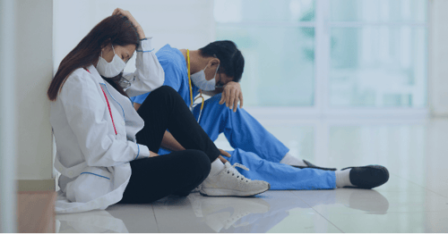 Two doctors sit sadly in a hallway